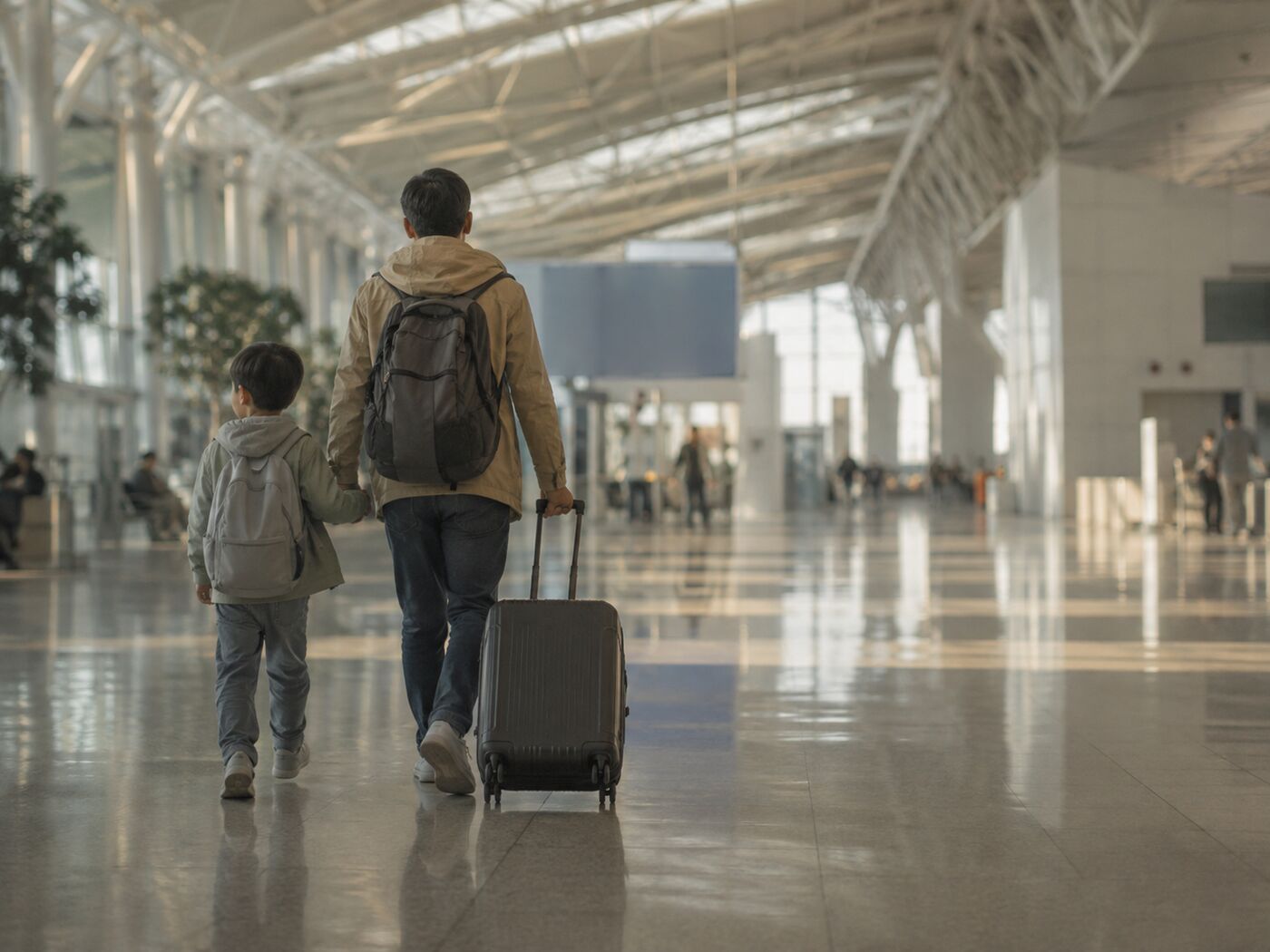 공항 출국장 홀에서 캐리어를 끌고 게이트 쪽으로 걸어가는 어른과 여덟 살쯤 되는 아이의 뒷모습